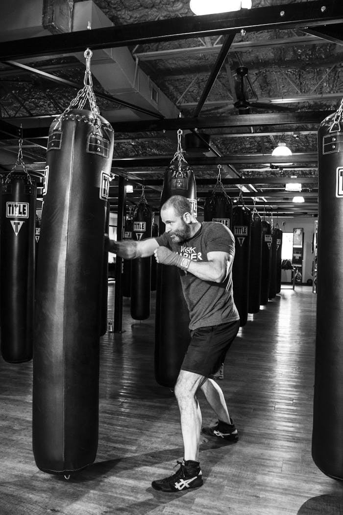 A man boxing with a punching bag in a gym, captured in black and white.